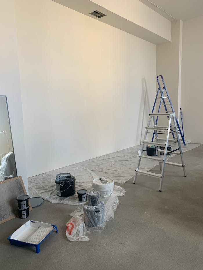 A room in the process of renovation with painting supplies and a ladder.